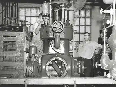 Historic photo of technicians operating industrial ammonia refrigeration equipment in a mechanical room.