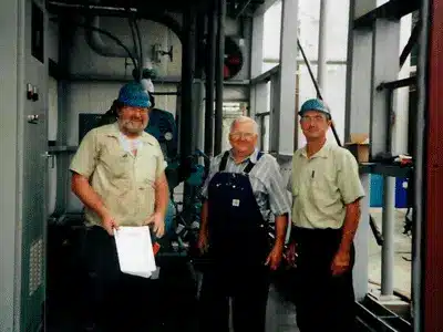 Three Banjo Refrigeration team members standing in an industrial facility, wearing work gear and hard hats.